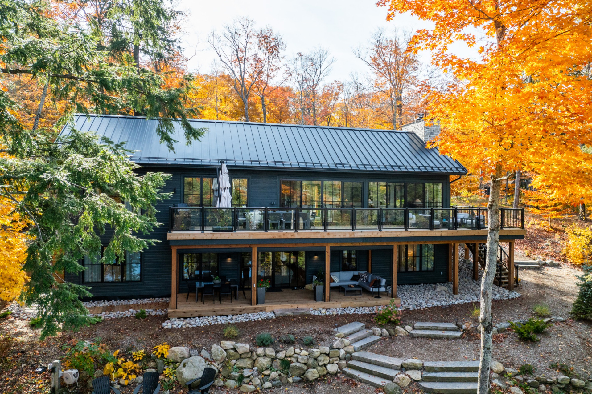 A dark-clad cottage with a glass-rail deck in autumn, built by Corbin Patten Designs